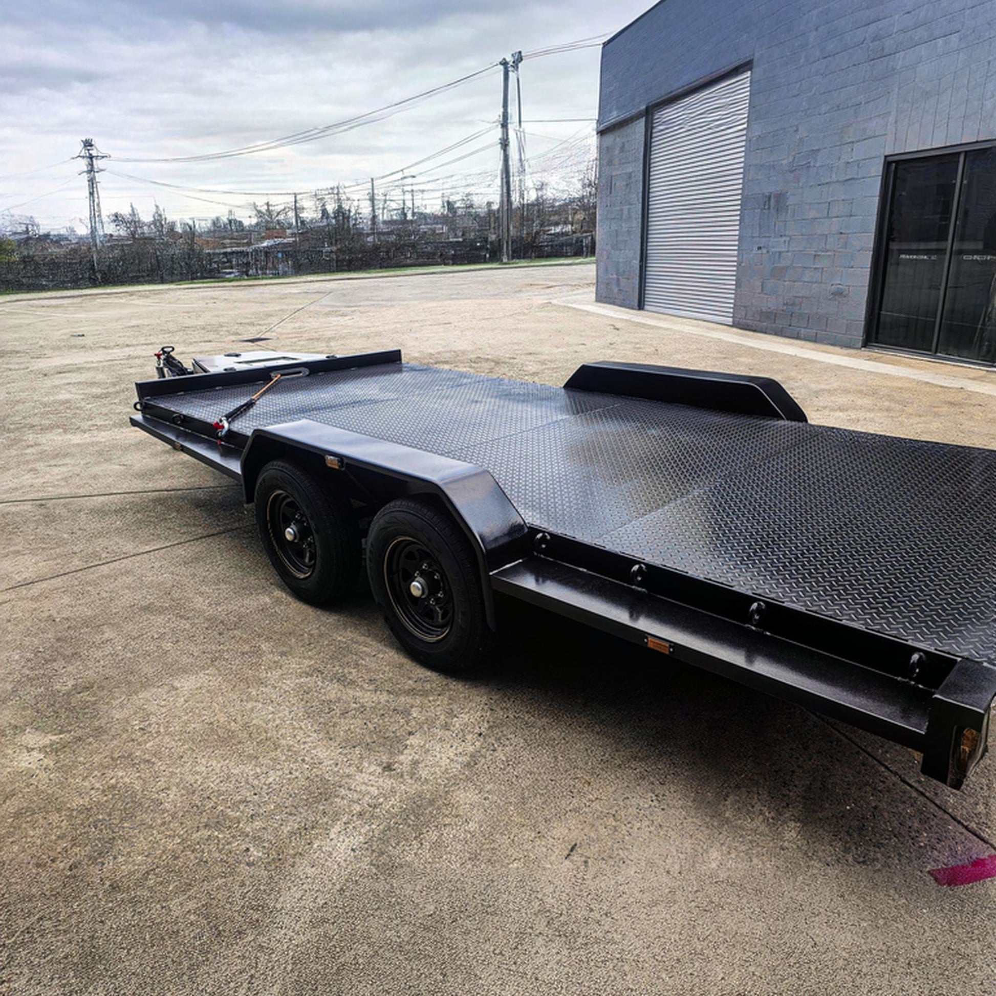 Trailer Hire Brisbane - Black metal flatbed trailer on a concrete surface with a building in the background