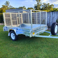 cage trailer hire Brisbane​ - Metal trailer with a cage on grass, with trees and a fence in the background