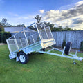 cage trailer hire Brisbane​ - Metal trailer with a cage on a grassy area under a blue sky with clouds.