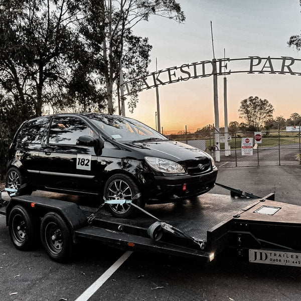 Black car on a trailer with 'Lakeside Park' sign in the background - JD Car Trailer Hire