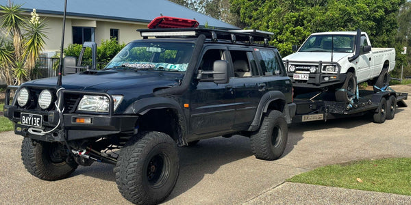 Black off-road vehicle towing a white truck on a driveway by a car trailer hire