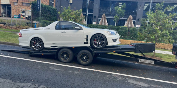 White car on a flatbed car trailer hire in an urban setting
