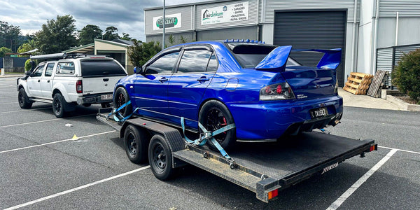 Blue car on a car trailer hire in a parking lot with a building in the background