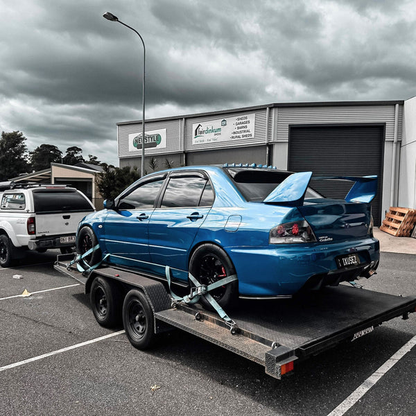 Trailer Hire Brisbane - Blue car on a trailer in front of a building with a cloudy sky.