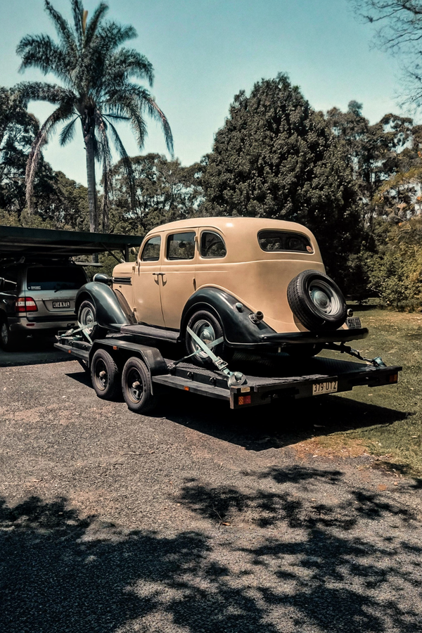Vintage car on a trailer with a palm tree and trees in the background with JD Trailer Hire
