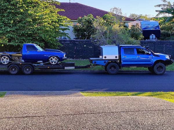 Blue truck towing a blue car on a trailer in a residential area - JD Trailer Hire - Car Trailer Hire Brisbane